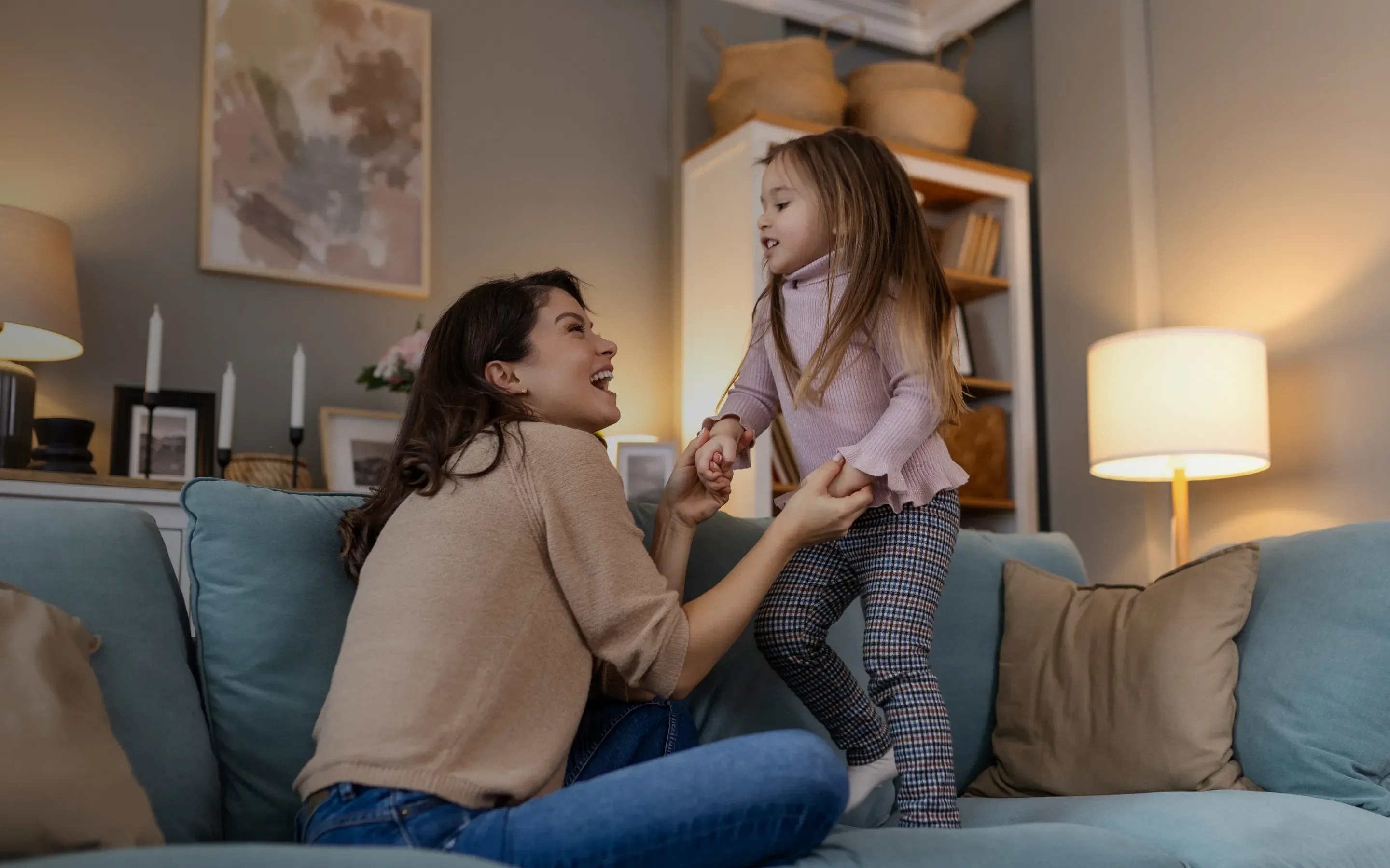 Image with mother and daughter playing on the sofa with a lot of surrounding lights open.